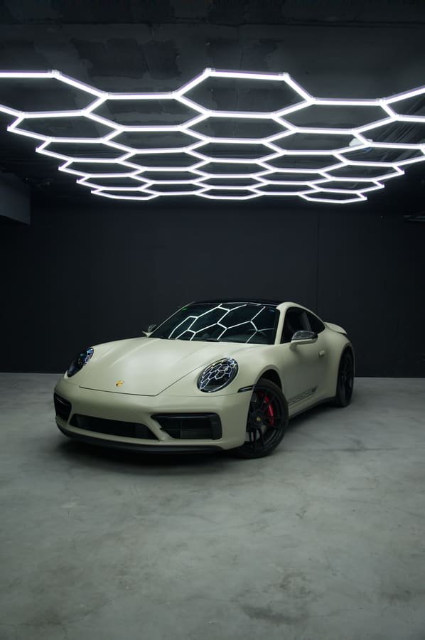 Porsche 911 Carrera GTS con Car Wrap arena satinado, tres cuartos delantero bajo las luces hexagonales del estudio