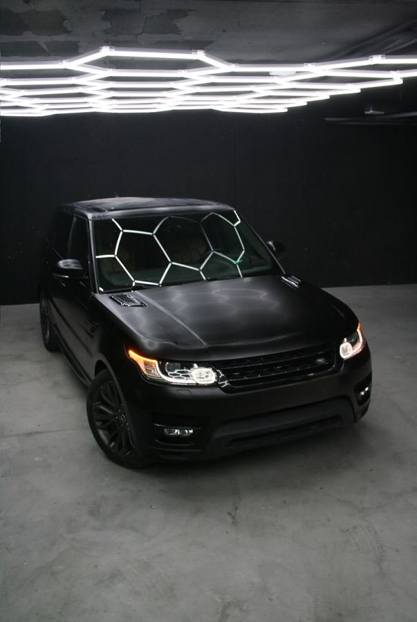 Range Rover Sport con Car Wrap negro satinado, tres cuartos delantero bajo las luces hexagonales del estudio