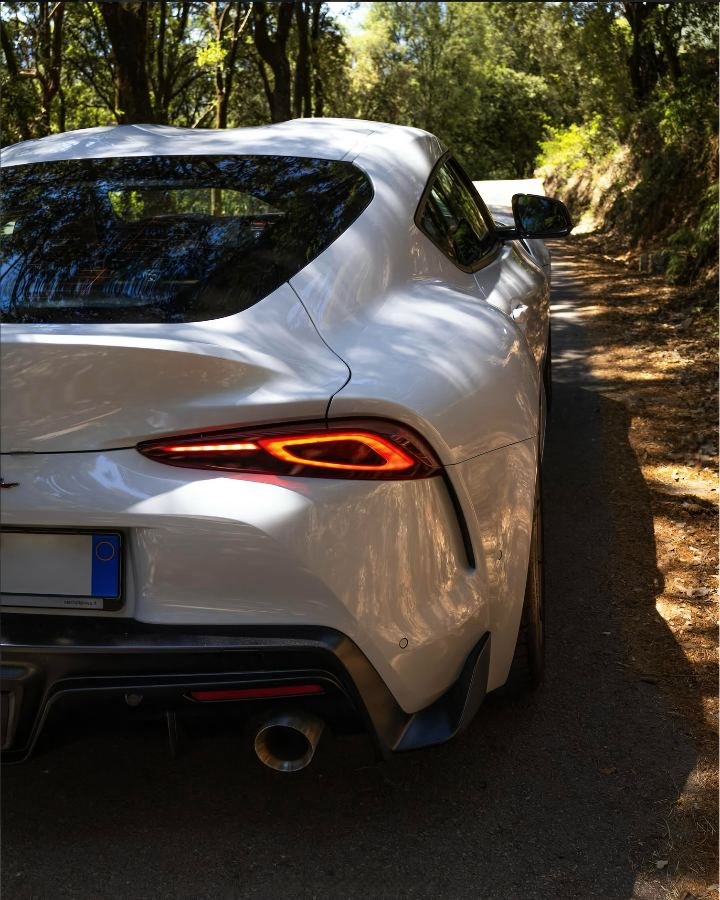 White Toyota GR Supra rear quarter on a tree-lined mountain road